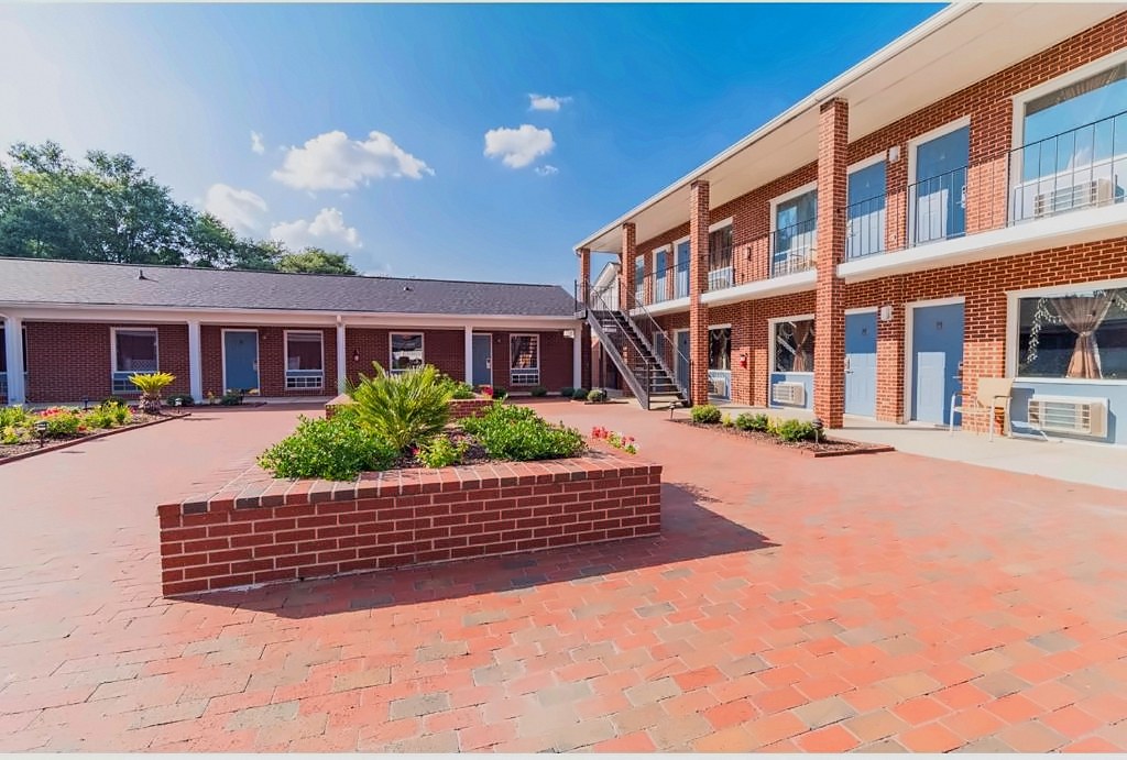 The sunny brick courtyard at Winton Inn & Suites, with garden beds and two-story guest buildings